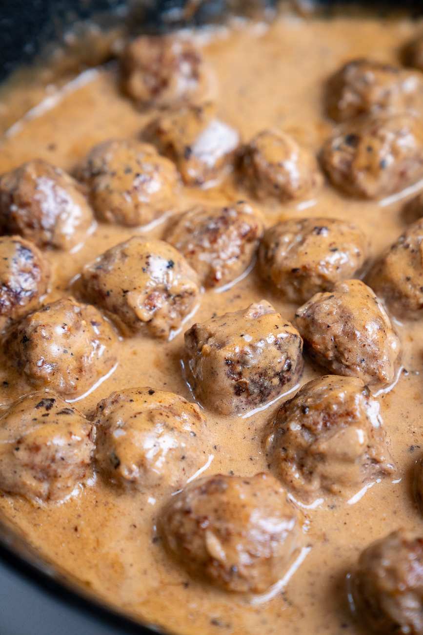 Mini Swedish meatballs with a glossy brown glaze, paired with a creamy sauce on a white plate