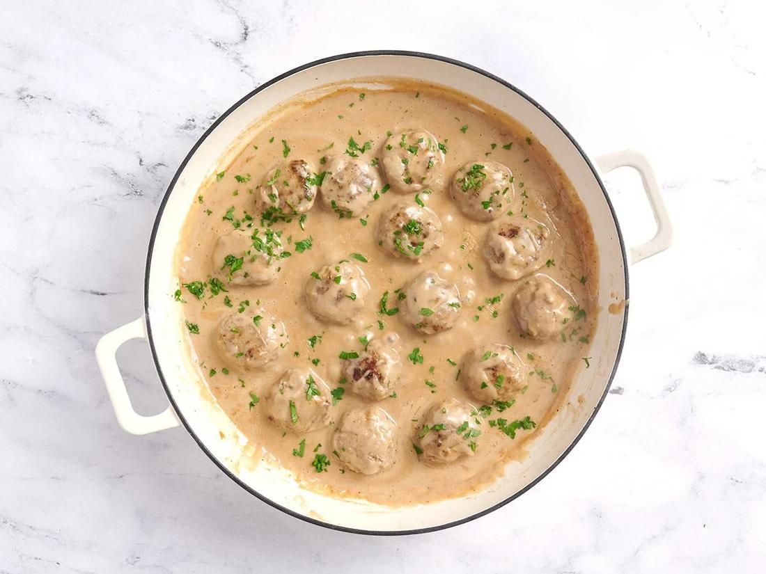 Homestyle Swedish meatballs simmering in a cast iron skillet with rich blonde pan gravy and fresh parsley