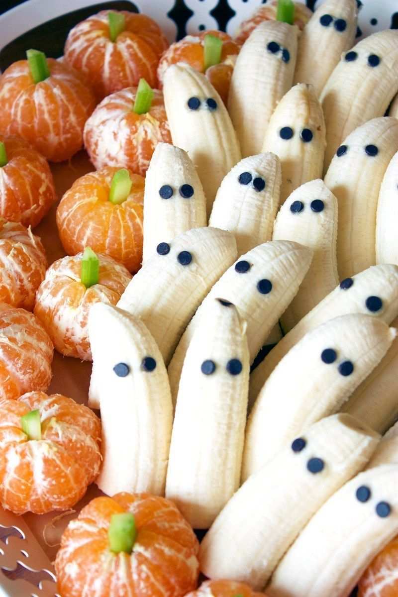 Banana halves with chocolate eyes and clementine “pumpkin” slices arranged on a colorful fruit platter.
