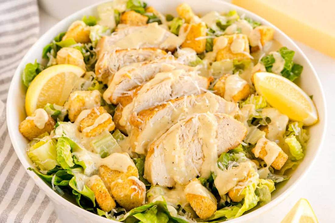 Lemon herb grilled chicken caesar salad sliced on top of crisp romaine with shaved parmesan