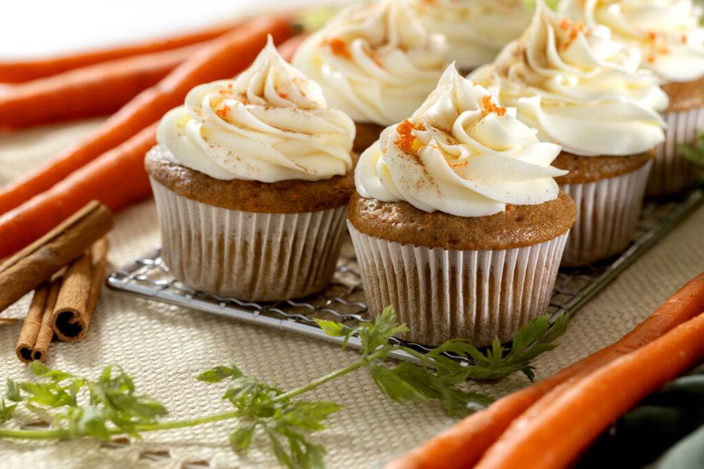Fluffy carrot cupcake with a generous swirl of pink cream cheese frosting and chopped pecans