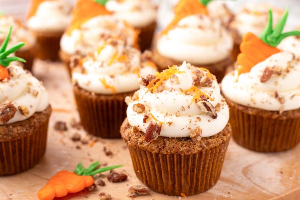 Large batch of moist carrot cake cupcakes topped with thick cream cheese frosting and toasted pecans