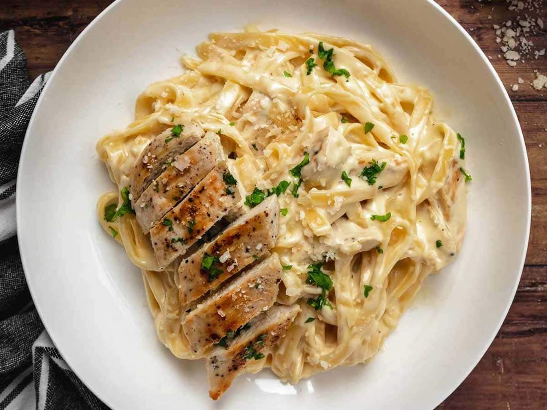 Gluten-free chicken alfredo featuring tender sliced chicken breast and silky parmesan cream sauce over fettuccine.