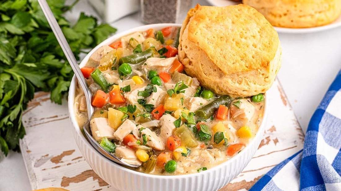 Slow cooker chicken pot pie soup with tender chicken, peas, carrots, potatoes, and flaky biscuit topping
