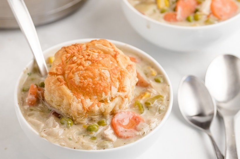 Creamy chicken pot pie soup with chicken, peas, carrots, potatoes, and herb‑infused biscuit topping