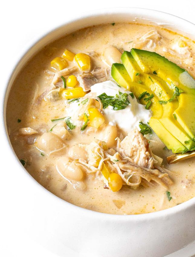 Salsa verde white chicken chili garnished with lime wedges and melted pepper jack cheese