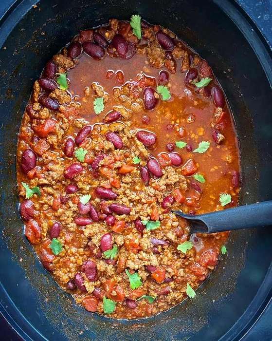 Slow‑cooked beef chili bowl with beans, melted cheese, sour cream, jalapenos, dark chocolate depth