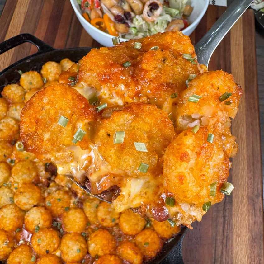 Chili tater tot casserole with beef, beans, melted cheese, sour cream, jalapenos, spicy queso drizzle