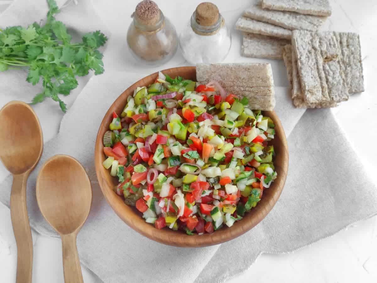 Colorful diced cucumber, red bell pepper, and tomato salsa in a festive bowl with lime wedges
