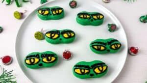 Green‑frosted peanut butter cookies shaped like Grinch faces with candy eyes and smiles