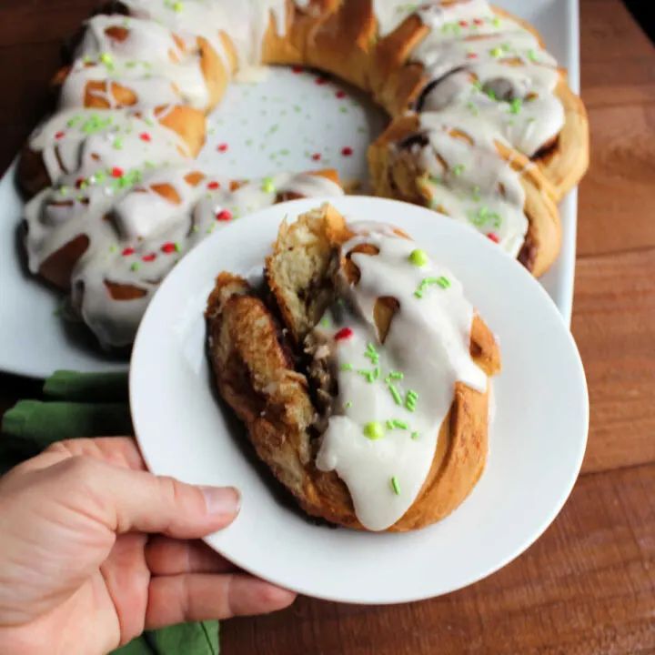 Circular wreath of cinnamon rolls glazed with icing, decorated with red berries