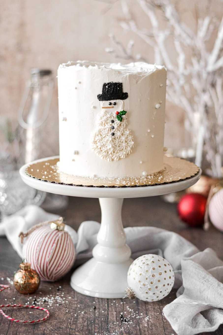White buttercream cake decorated with a smiling snowman, carrot nose, and chocolate eyes