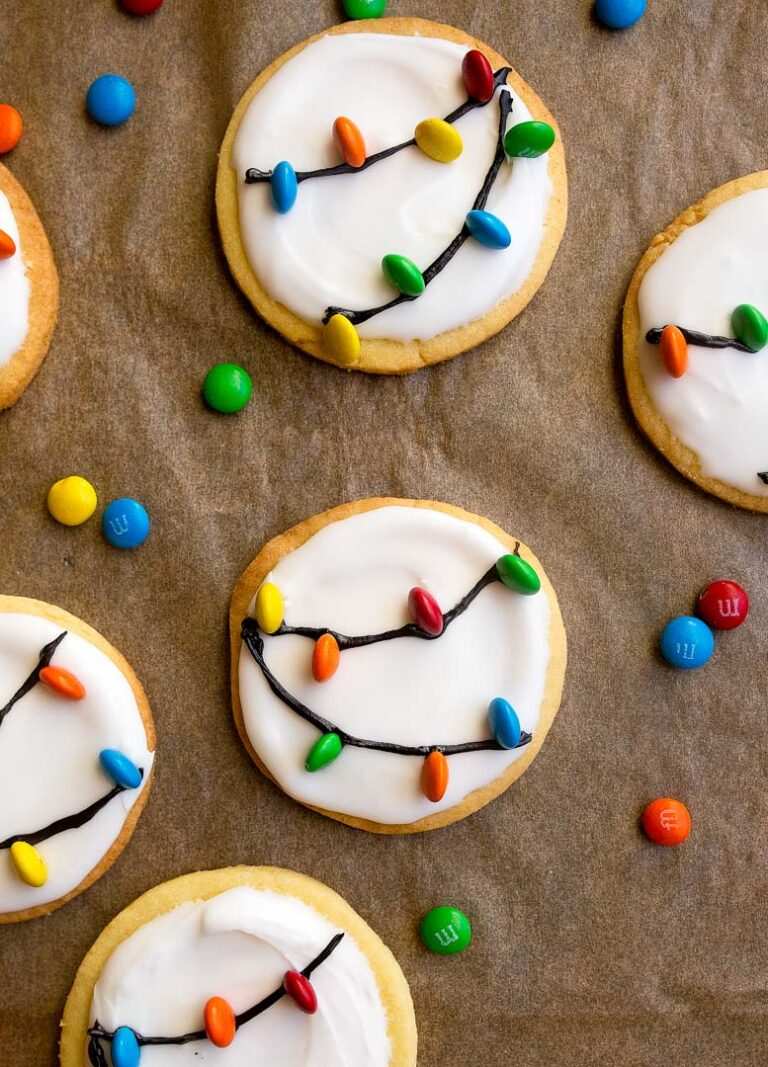 Sugar cookies decorated to look like glowing Christmas lights with icing and sprinkles on a table.