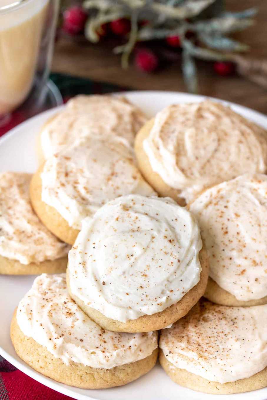 Spiced sugar cookies topped with a thick, creamy eggnog frosting on a white plate.
