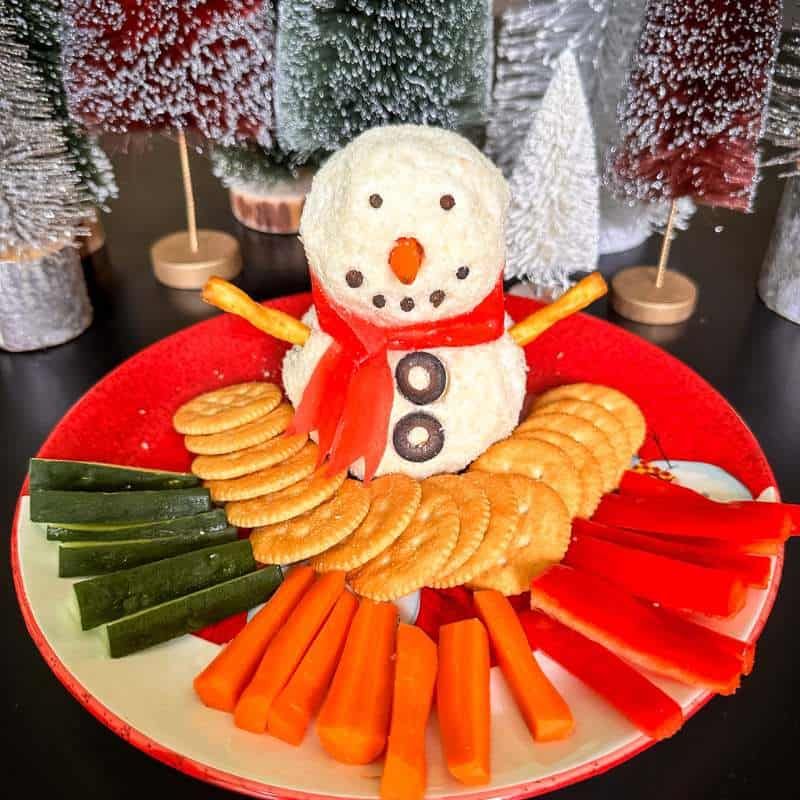Snowman-shaped cheese ball surrounded by crackers, carrots, and bell pepper sticks