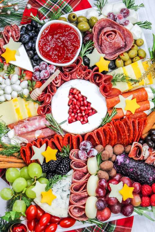 Elegant board featuring brie, sliced cured meats, pomegranate seeds, and rosemary sprigs