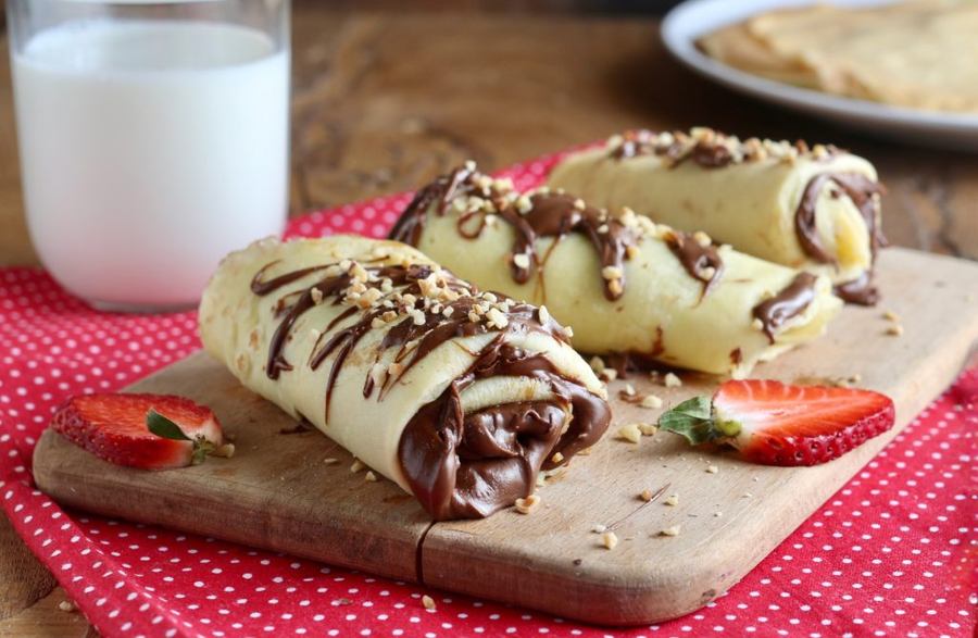 Rolled crepes filled with Nutella and chocolate, topped with powdered cocoa and sliced almonds