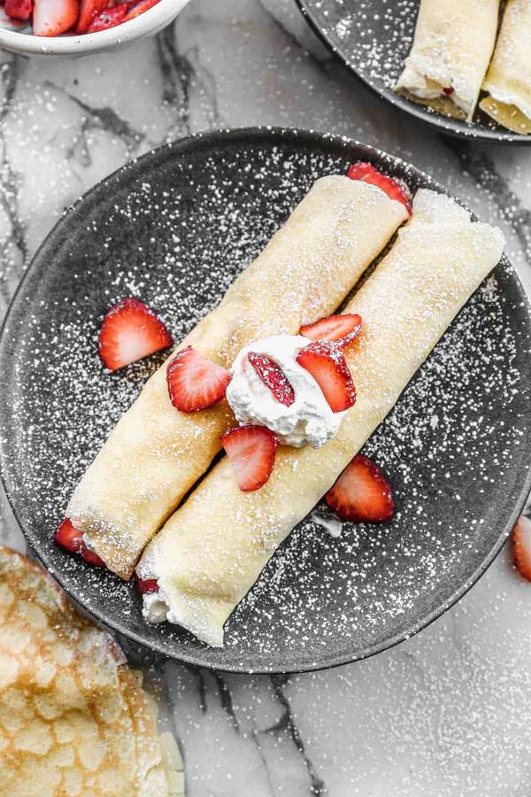Light golden crepes topped with strawberry‑swirled whipped cream and fresh strawberry halves