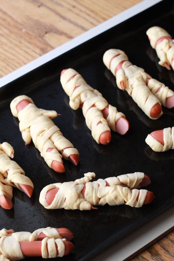 Golden crescent roll wrapped hot dogs with ketchup eyes and mustard mouths on a plate