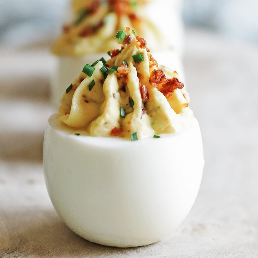 Classic deviled eggs with creamy yolk filling, smoky paprika, fresh chives, and crunchy bacon bits
