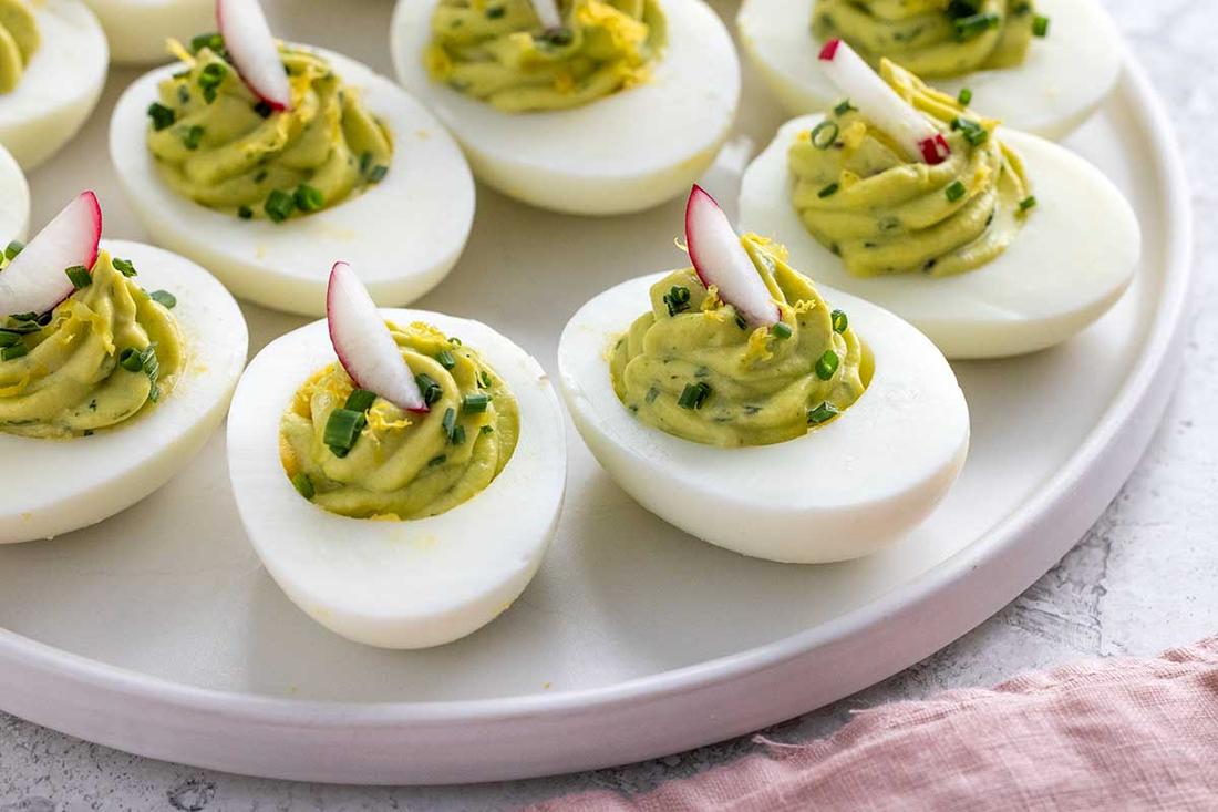 Avocado deviled eggs with silky yolk filling, lime zest, chives, and smoked paprika