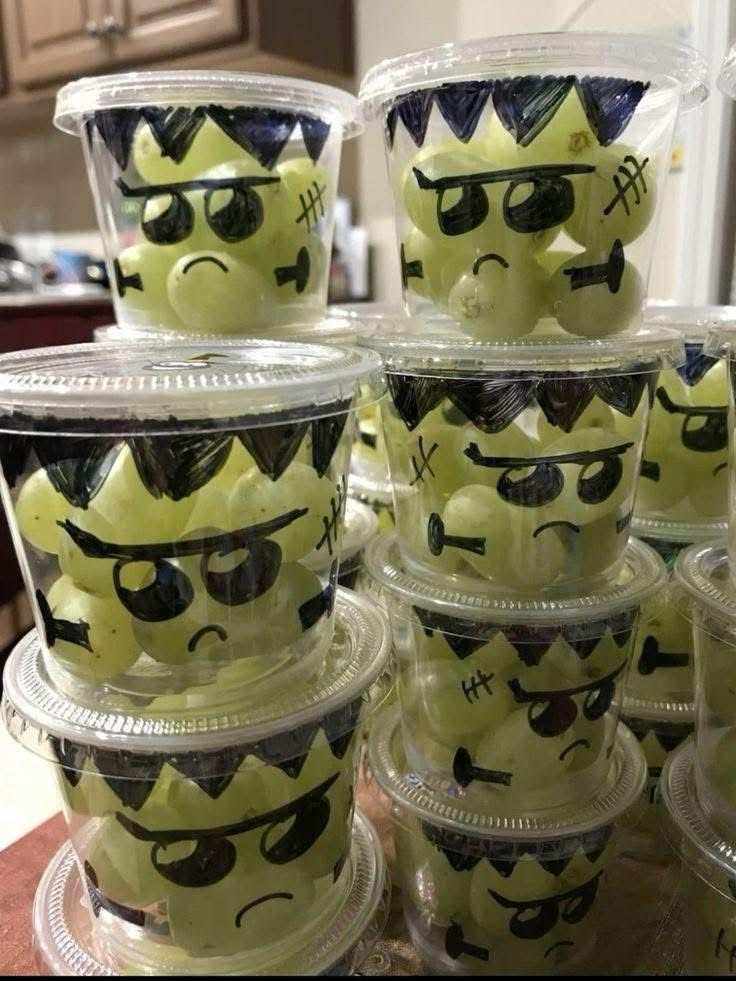 Mini clear cups filled with green grapes, chocolate “scar” lines, and gummy eye patches, resembling Frankenstein’s face.