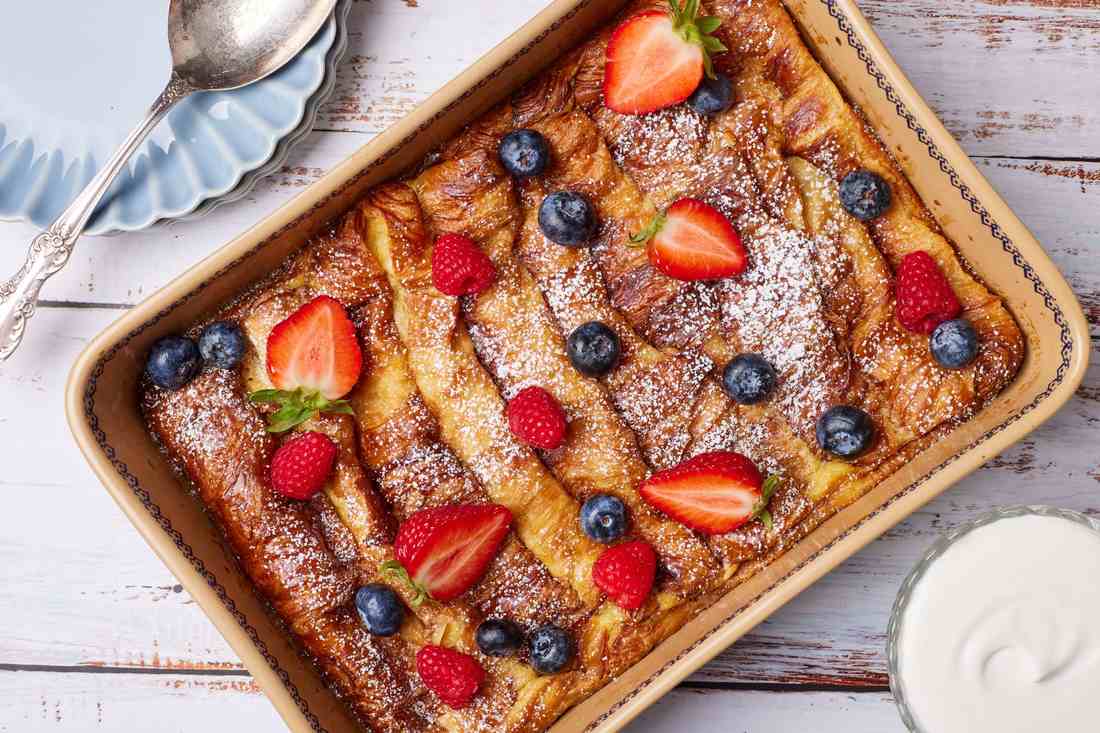 Fluffy croissant French toast casserole with buttery layers, golden crust, and a drizzle of honey