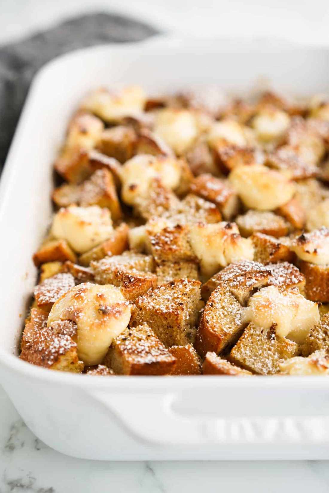 Cream cheese French toast casserole featuring golden bread cubes, fresh berry compote, and a dusting of powdered sugar