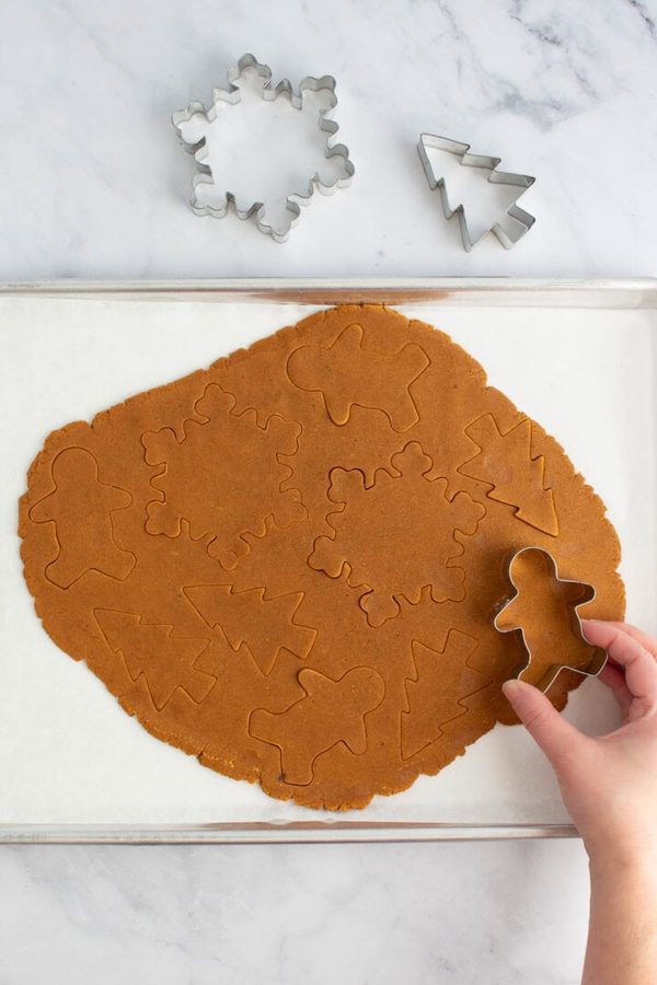 Rolling gingerbread dough with holiday cookie cutters, warm spices, festive shapes