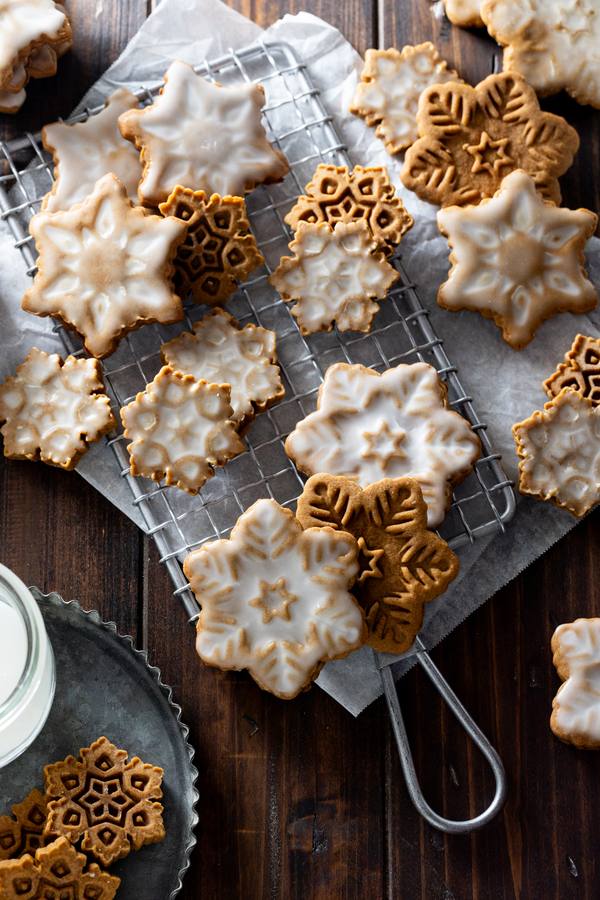 Snowflake-shaped gingerbread cookies iced with white royal icing, speckled sugar, warm spices