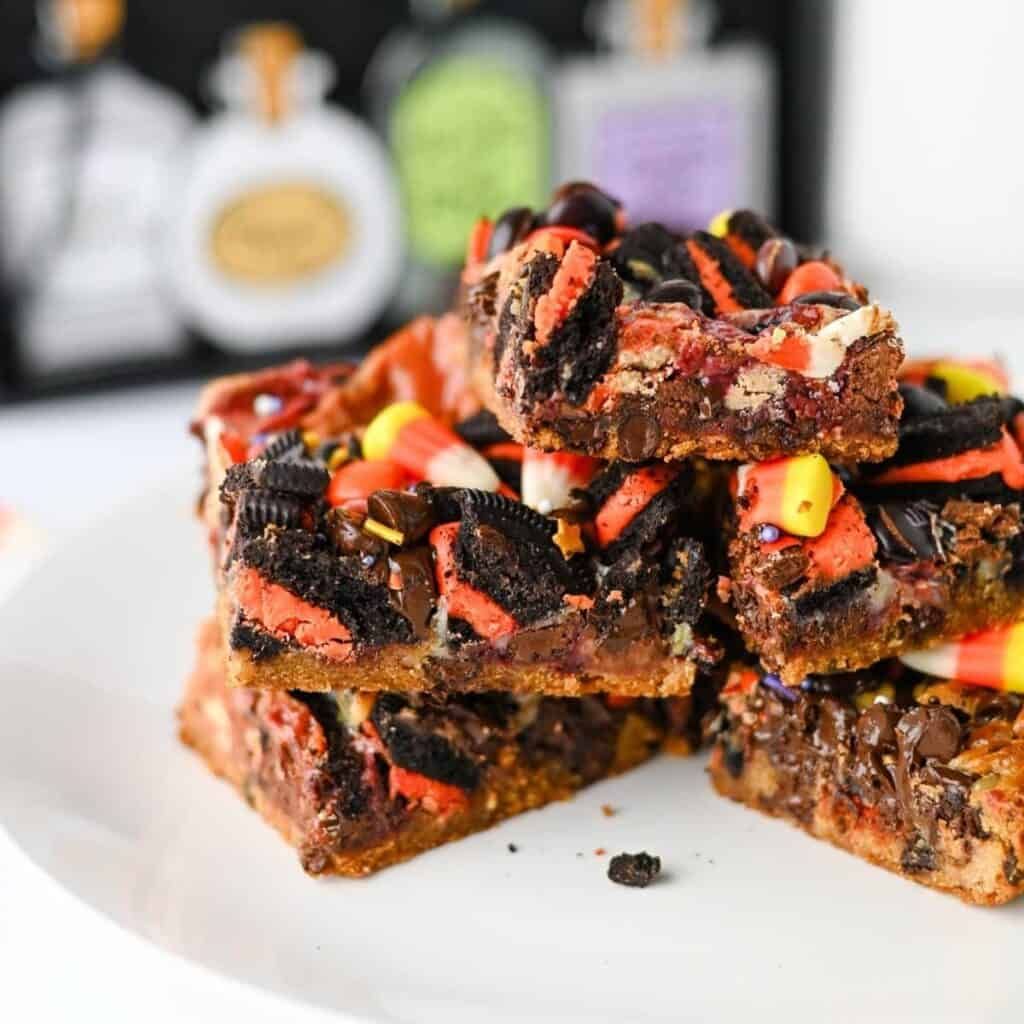 Layered dessert bar squares with graham crust, chocolate chips, coconut, orange sprinkles, and gummy worms.