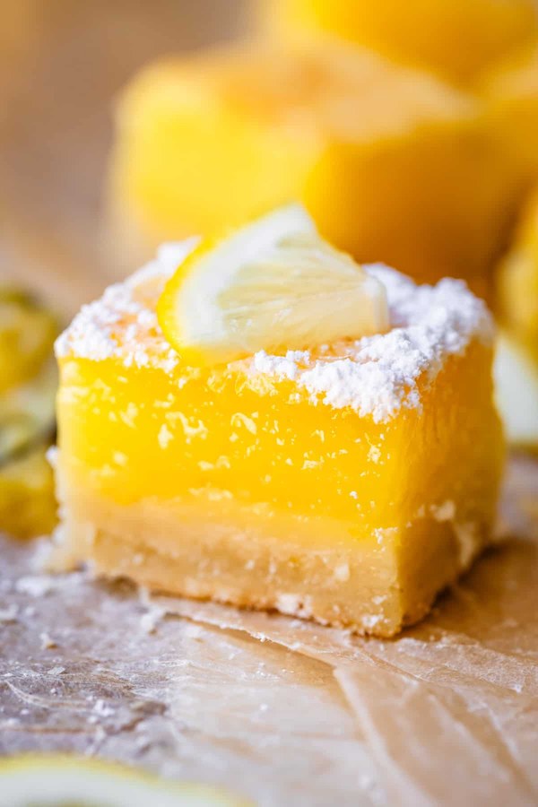 Lemon squares with almond topping, bright yellow, dusted with powdered sugar, on a wooden board