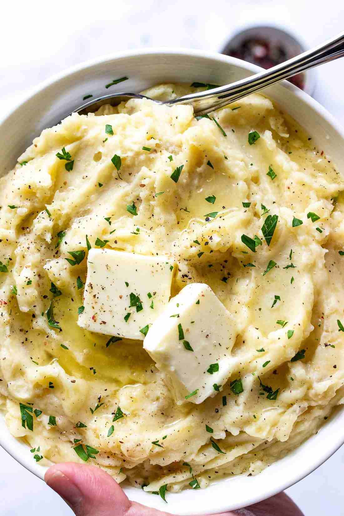 Decadent slow cooker mashed potatoes whipped with melted cream cheese and golden butter in ceramic bowl
