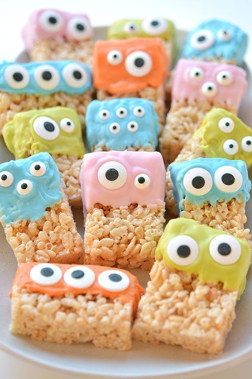 Green‑colored Rice Krispies squares topped with candy eyes and chocolate “teeth” on a spooky tray.