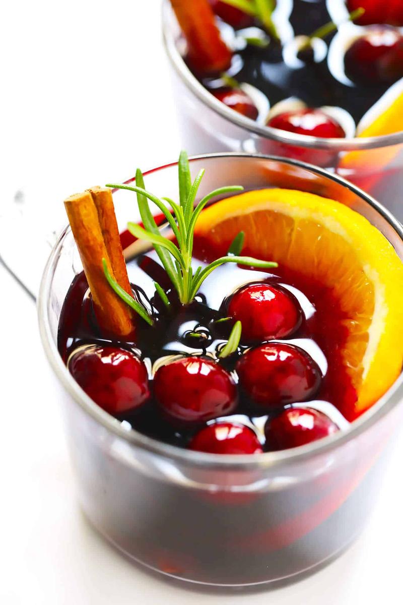 Cranberry mulled wine with ruby-red wine, fresh orange slices, and cinnamon sticks in clear mugs.