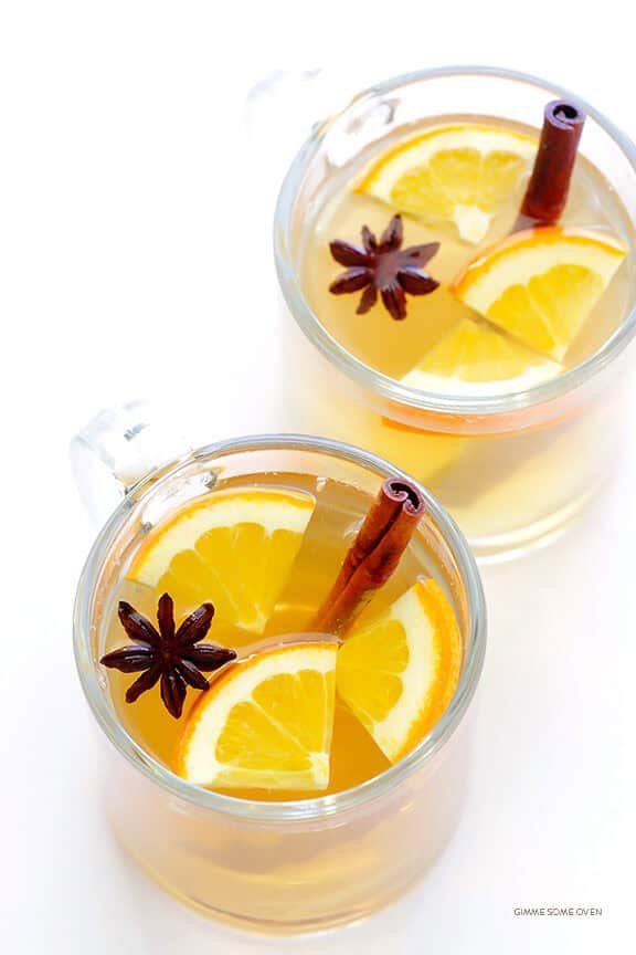 Warm apricot fig mulled white wine with dried fruits, orange slices, and cinnamon in clear mugs.