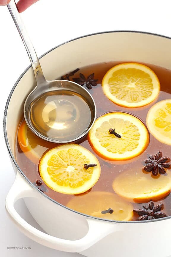 Peach star anise mulled white wine with orange slices, whole cinnamon, and spices in glass mugs.