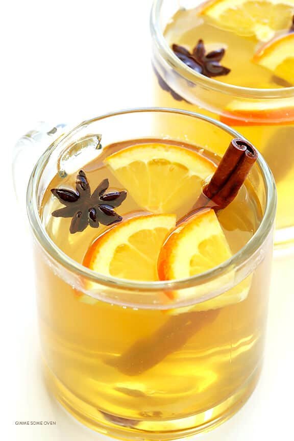 Chamomile citrus mulled white wine garnished with orange wheels, cinnamon sticks, and herbs in glass mugs.