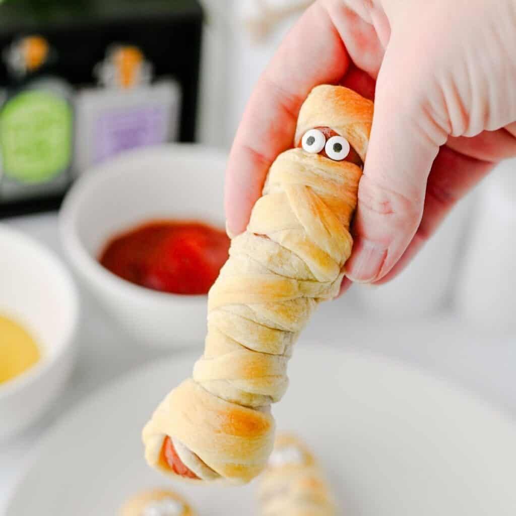 Cheesy pizza mummy roll-up finger food with candy eyes dipped in red marinara sauce.