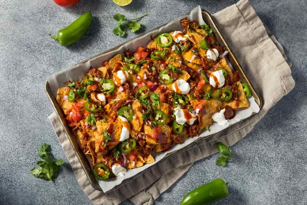 Crispy carnitas pork nachos smothered in melted cheese, fresh jalapeños, guacamole, sour cream, and crispy tortilla chips