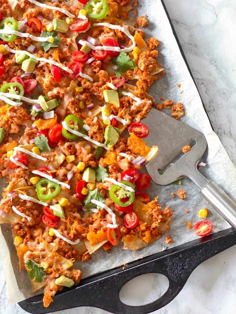 Triple cheese sheet pan nachos featuring melted cheddar, jack cheese, jalapeños, guacamole, and loaded tortilla chips