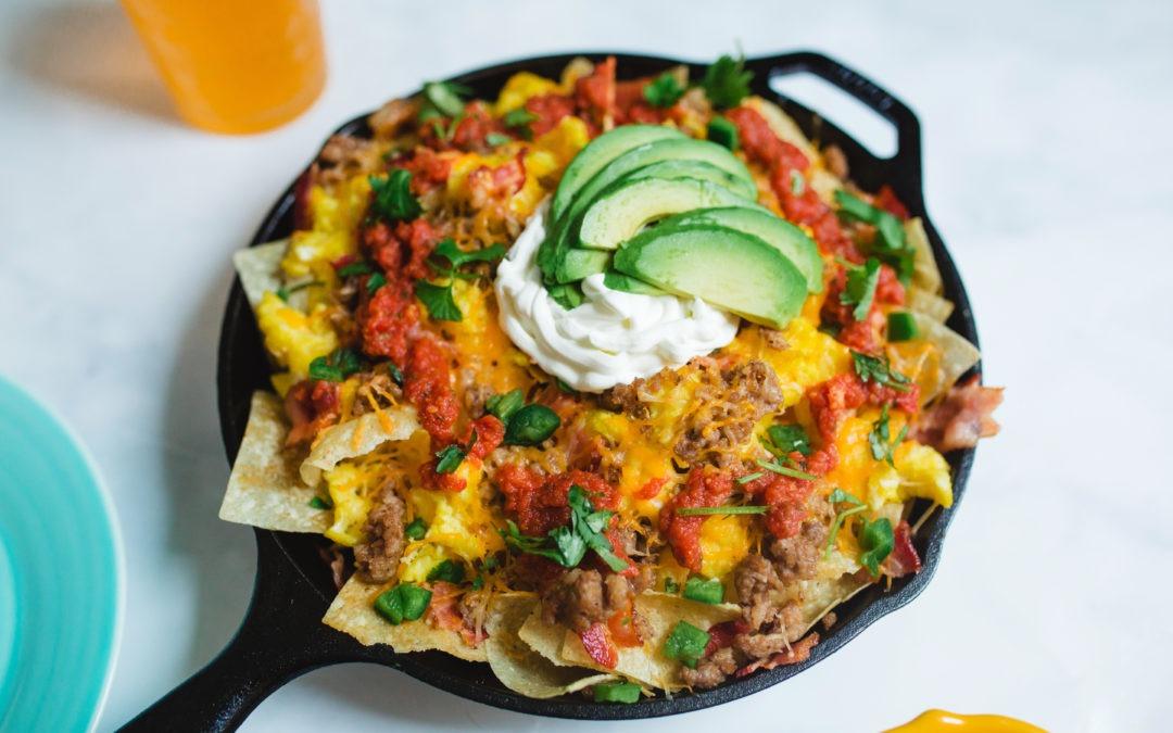 Morning breakfast nachos topped with fried eggs, melted cheese, jalapeños, guacamole, and crispy tortilla chips
