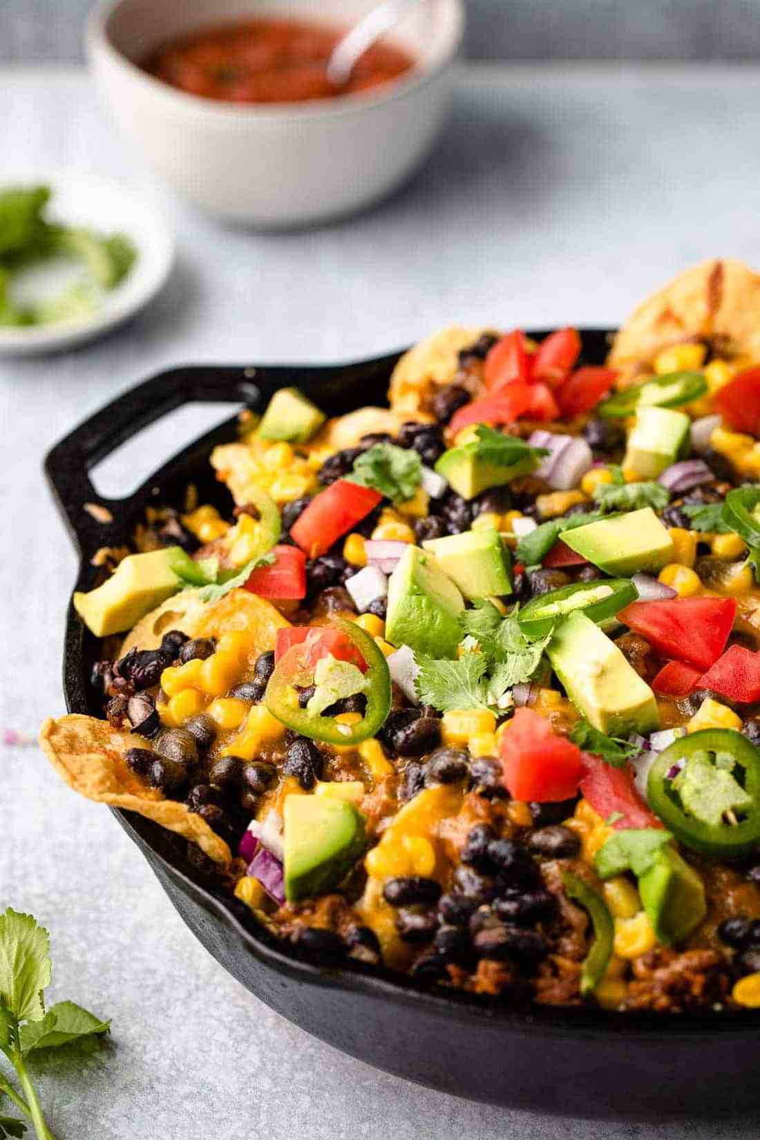 Sheet pan nachos covered in melted cheese, spicy jalapeños, fresh guacamole, sour cream, and crispy tortilla chips.