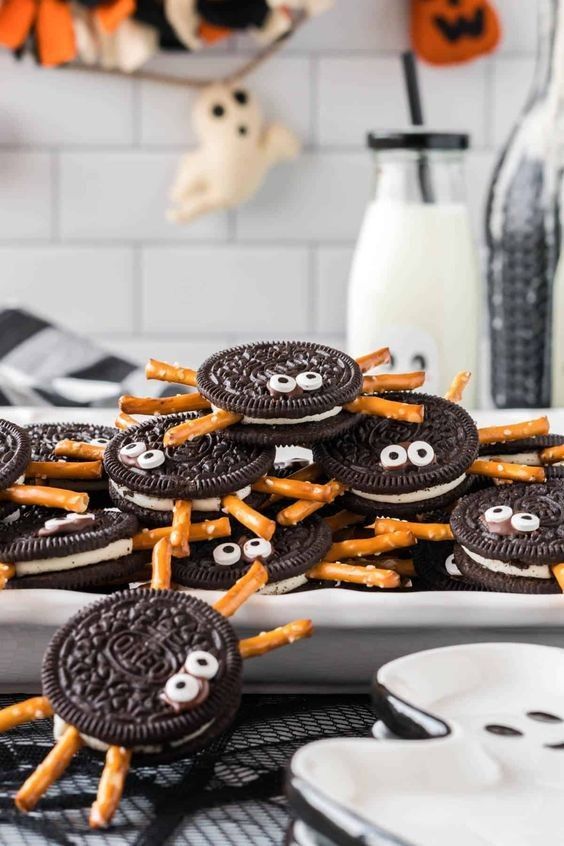 Oreo halves topped with chocolate “body” and pretzel sticks as spider legs, arranged on a dark platter.