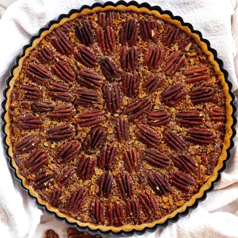 Rustic fluted pecan pie tart slice showing toasted pecans and golden caramel filling on plate