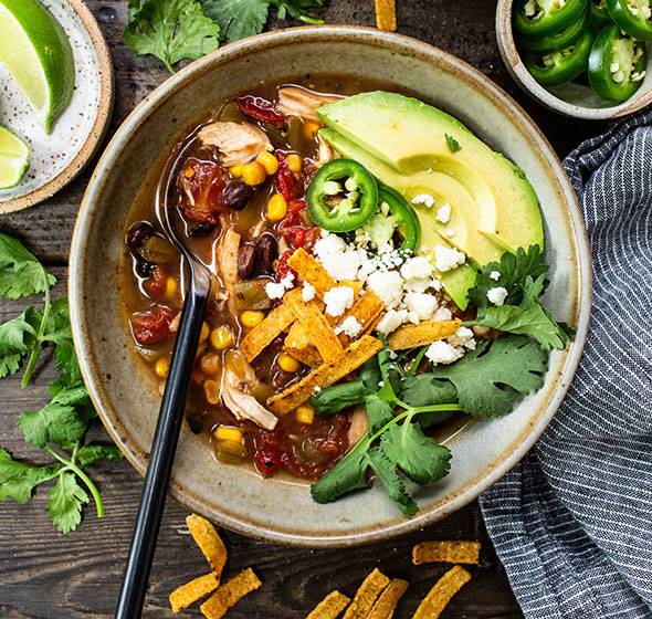 Hearty chicken tortilla soup with tomato broth, shredded chicken, crunchy tortillas, avocado, lime