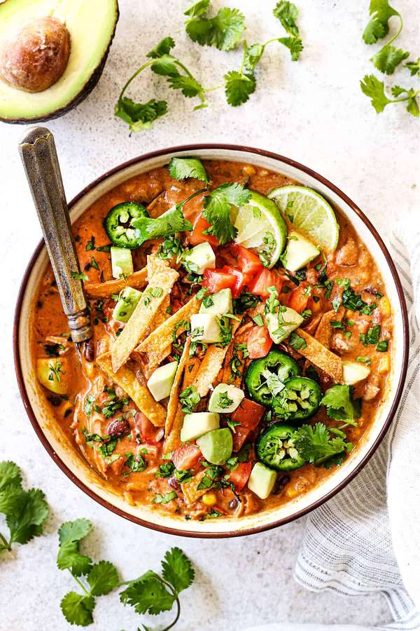 Creamy chicken tortilla soup with velvety broth, shredded chicken, crispy tortilla strips, avocado, lime