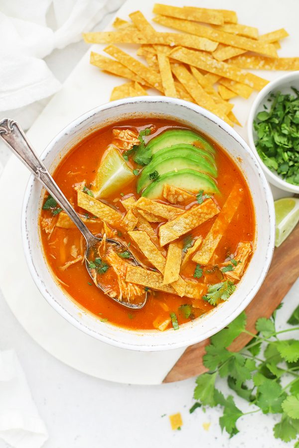 Classic chicken tortilla soup with rich tomato broth, shredded chicken, crispy tortilla strips, avocado, and lime