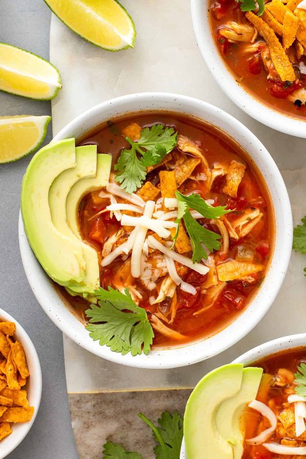 Chicken tortilla soup with roasted red peppers, tomato broth, shredded chicken, crunchy tortilla strips, avocado garnish