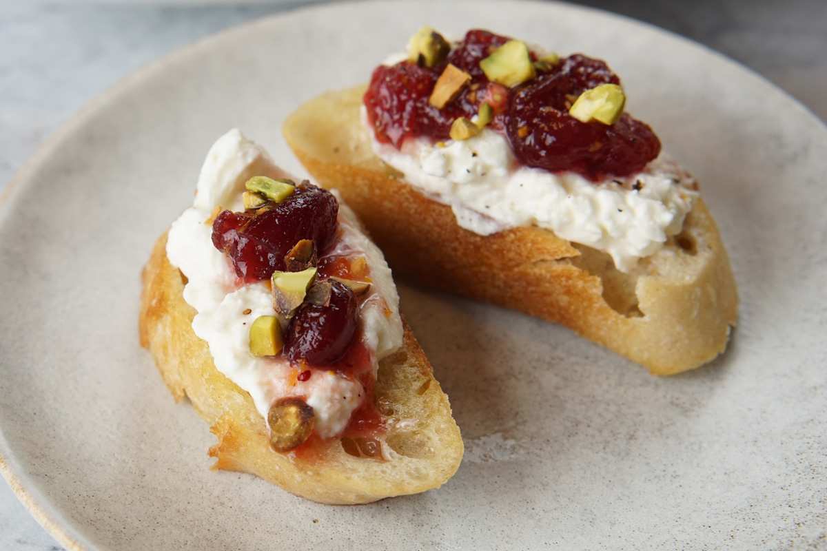 Toasted crostini topped with ricotta, cranberry sauce, and crushed pistachios